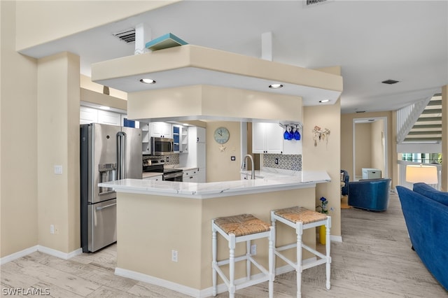 kitchen with kitchen peninsula, light hardwood / wood-style flooring, white cabinetry, decorative backsplash, and stainless steel appliances