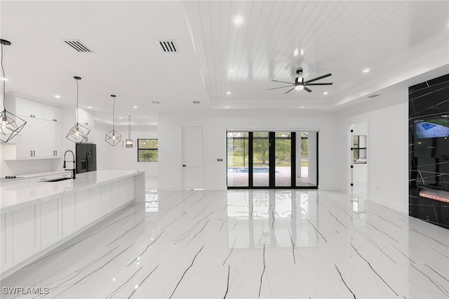 unfurnished living room featuring wood ceiling, a tray ceiling, ceiling fan, and sink