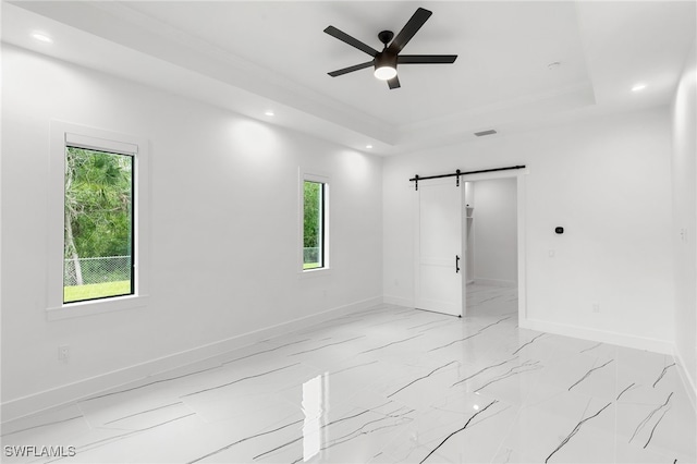 unfurnished room featuring a barn door, a tray ceiling, and ceiling fan