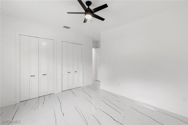 unfurnished bedroom featuring ceiling fan and multiple closets