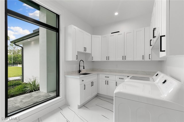 clothes washing area with cabinets, washer and clothes dryer, a healthy amount of sunlight, and sink