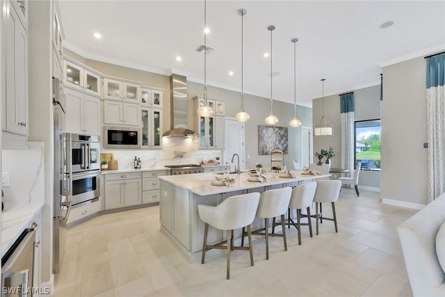 kitchen with a breakfast bar, a center island with sink, hanging light fixtures, wall chimney exhaust hood, and built in microwave