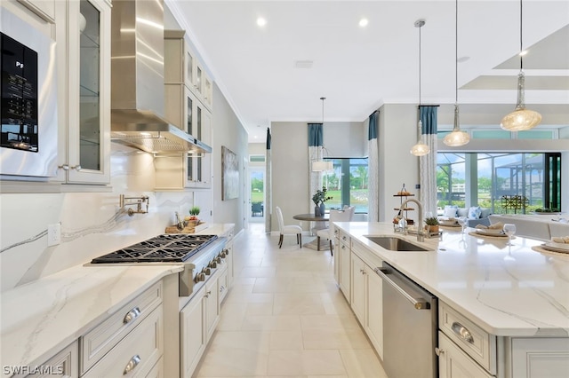 kitchen with sink, wall chimney exhaust hood, light stone counters, decorative light fixtures, and appliances with stainless steel finishes