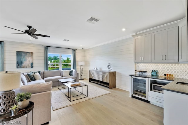 living room featuring light wood-type flooring, beverage cooler, wooden walls, crown molding, and ceiling fan