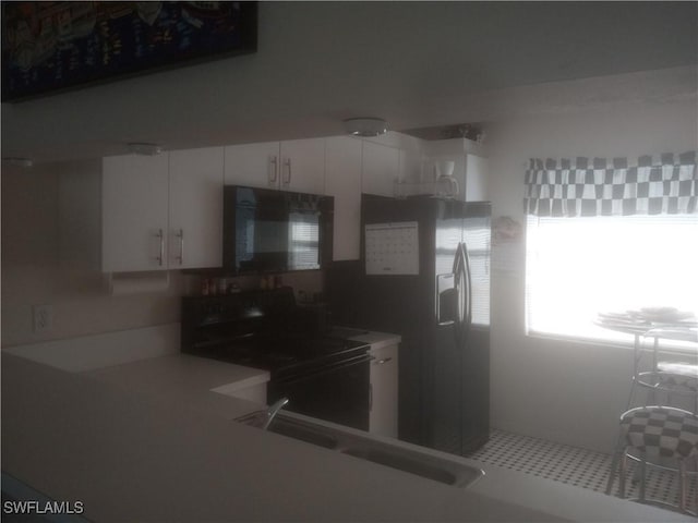 kitchen featuring white cabinets, stainless steel fridge, black range with electric stovetop, and sink