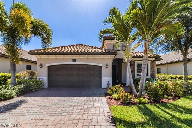 mediterranean / spanish-style house with stucco siding, an attached garage, a tile roof, and decorative driveway