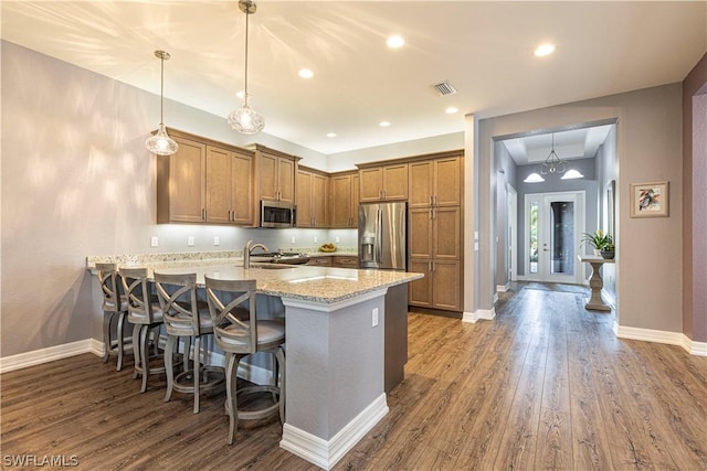 kitchen featuring a breakfast bar, hanging light fixtures, light stone counters, wood-type flooring, and stainless steel appliances