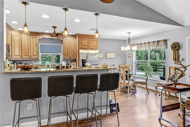 kitchen with stainless steel appliances, a wealth of natural light, light stone counters, and kitchen peninsula