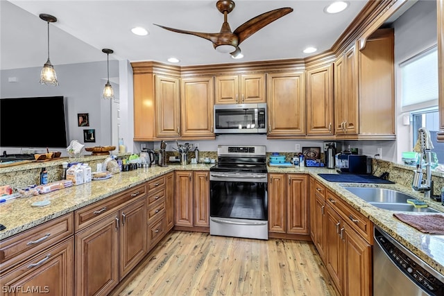 kitchen with sink, appliances with stainless steel finishes, light stone countertops, decorative light fixtures, and light wood-type flooring