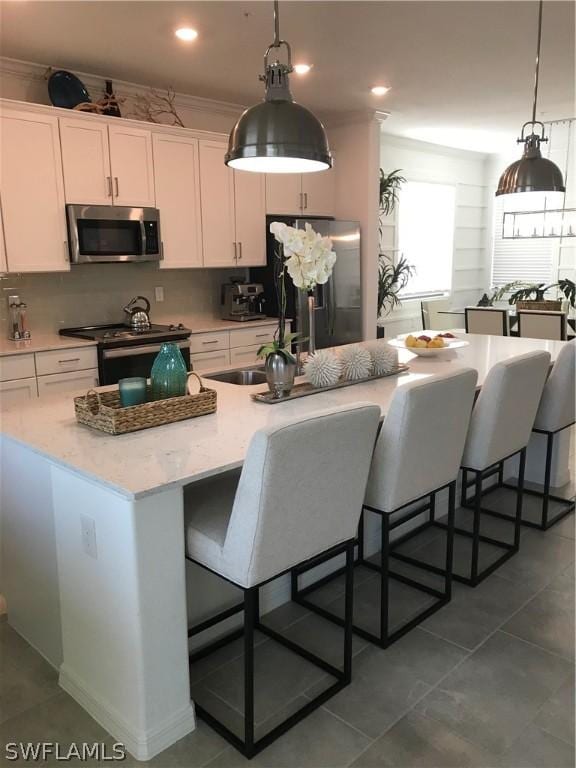 kitchen with white cabinets, a breakfast bar, a center island with sink, and appliances with stainless steel finishes