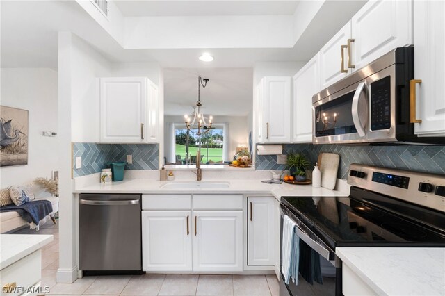 kitchen with tasteful backsplash, stainless steel appliances, light tile floors, hanging light fixtures, and white cabinetry