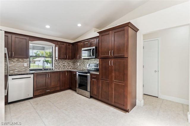 kitchen with lofted ceiling, dark stone countertops, decorative backsplash, sink, and stainless steel appliances