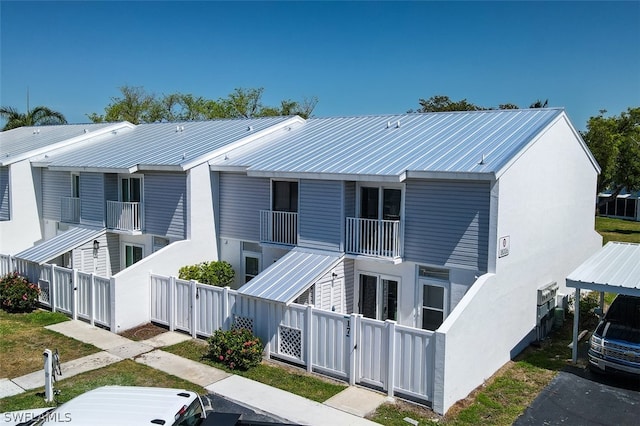 back of property with a fenced front yard, stucco siding, a gate, metal roof, and a balcony