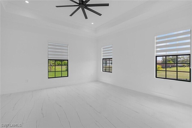 empty room with a tray ceiling, a wealth of natural light, and ceiling fan