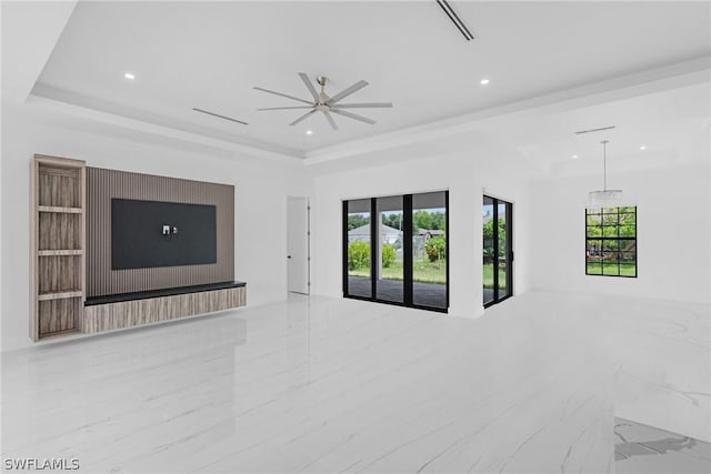 unfurnished living room with ceiling fan, a healthy amount of sunlight, and a tray ceiling