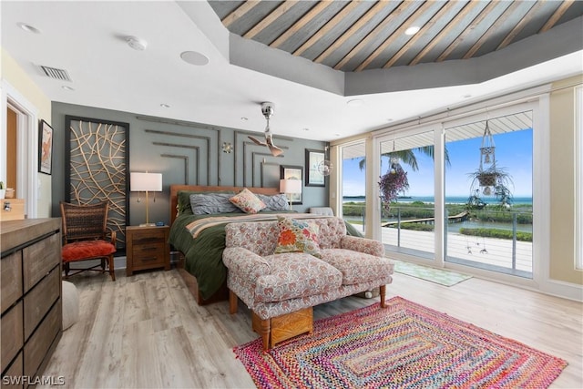 bedroom with expansive windows, a water view, access to exterior, and light hardwood / wood-style floors