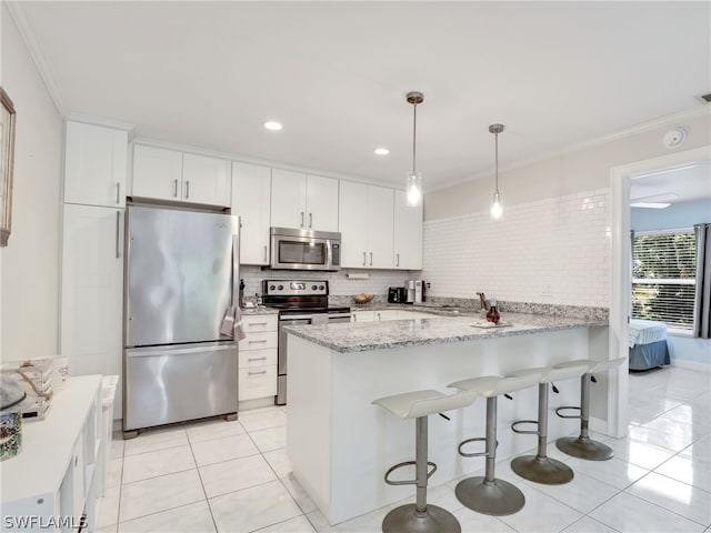 kitchen with kitchen peninsula, hanging light fixtures, ornamental molding, appliances with stainless steel finishes, and white cabinetry