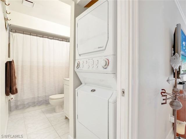 full bath featuring visible vents, a shower with shower curtain, toilet, stacked washing maching and dryer, and tile patterned flooring