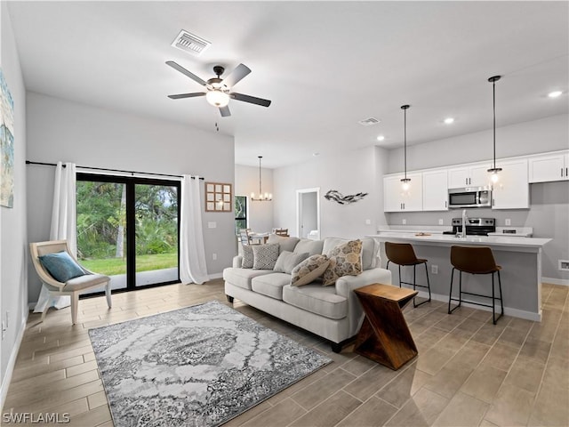 living room with ceiling fan with notable chandelier and light hardwood / wood-style flooring