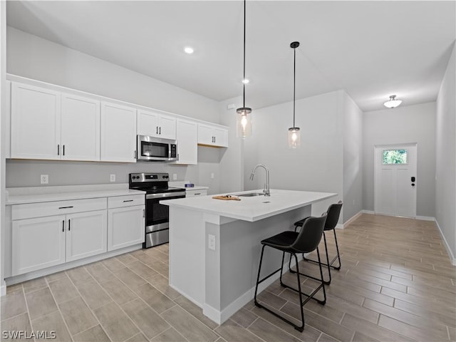 kitchen with appliances with stainless steel finishes, a kitchen island with sink, sink, pendant lighting, and white cabinets