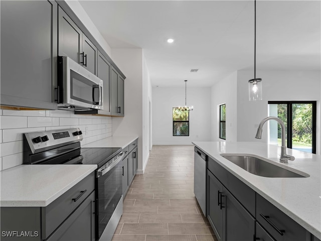 kitchen featuring stainless steel appliances, hanging light fixtures, sink, gray cabinetry, and light stone countertops