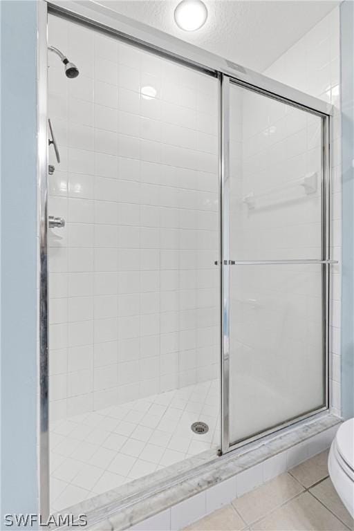 bathroom with tile patterned flooring, toilet, walk in shower, and a textured ceiling