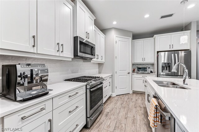 kitchen with light hardwood / wood-style floors, hanging light fixtures, white cabinetry, stainless steel appliances, and backsplash