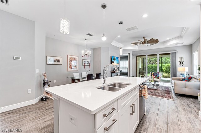 kitchen with a center island with sink, ceiling fan with notable chandelier, white cabinets, sink, and a raised ceiling