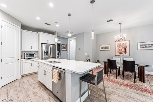 kitchen with stainless steel appliances, white cabinets, light wood-type flooring, and decorative light fixtures