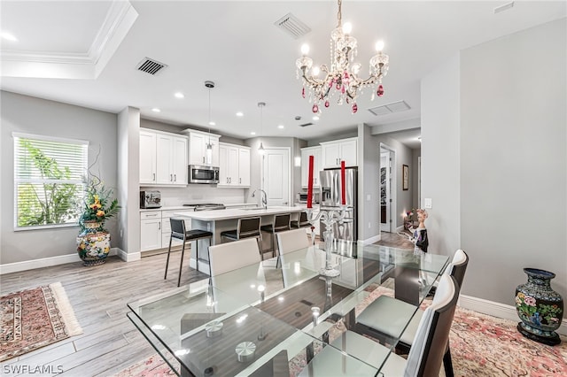 dining room with ornamental molding, light hardwood / wood-style flooring, a tray ceiling, a notable chandelier, and sink