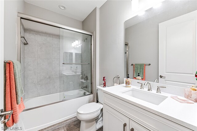 full bathroom with wood-type flooring, combined bath / shower with glass door, toilet, and vanity with extensive cabinet space