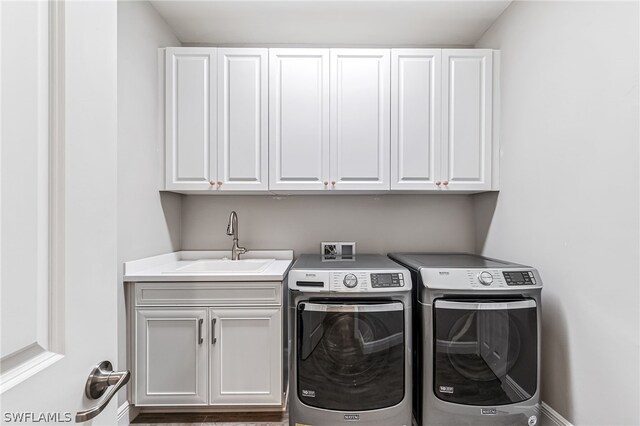 clothes washing area featuring hardwood / wood-style floors, washer hookup, sink, washer and clothes dryer, and cabinets