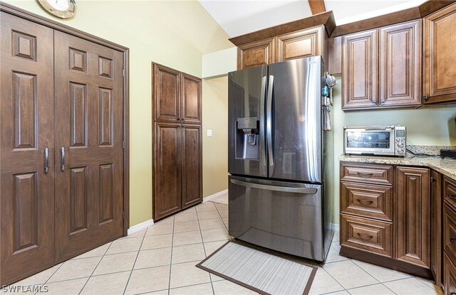 kitchen featuring light tile patterned floors, stainless steel refrigerator with ice dispenser, light stone countertops, and vaulted ceiling