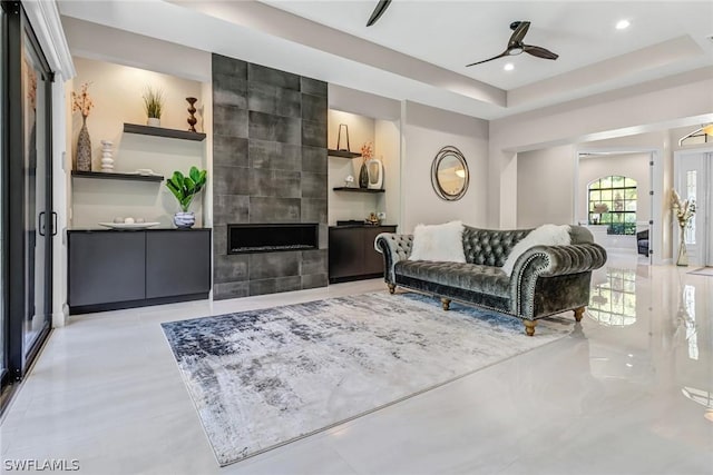 living room with ceiling fan, a fireplace, and a tray ceiling