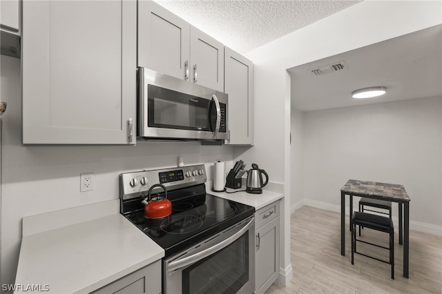 kitchen with appliances with stainless steel finishes, light hardwood / wood-style floors, a textured ceiling, and gray cabinets