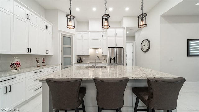 kitchen featuring backsplash, a kitchen island with sink, sink, white cabinets, and stainless steel fridge with ice dispenser