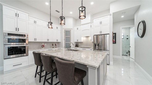 kitchen with appliances with stainless steel finishes, decorative light fixtures, white cabinetry, and an island with sink