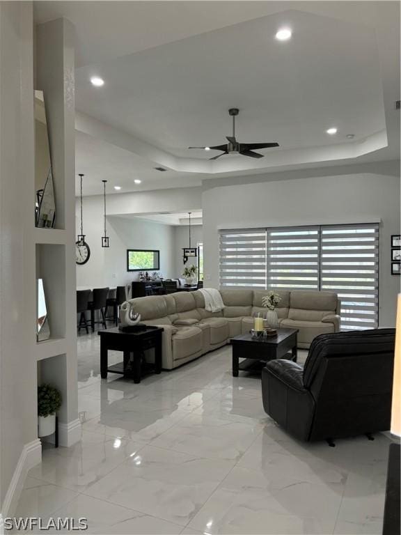 living room with a raised ceiling and ceiling fan