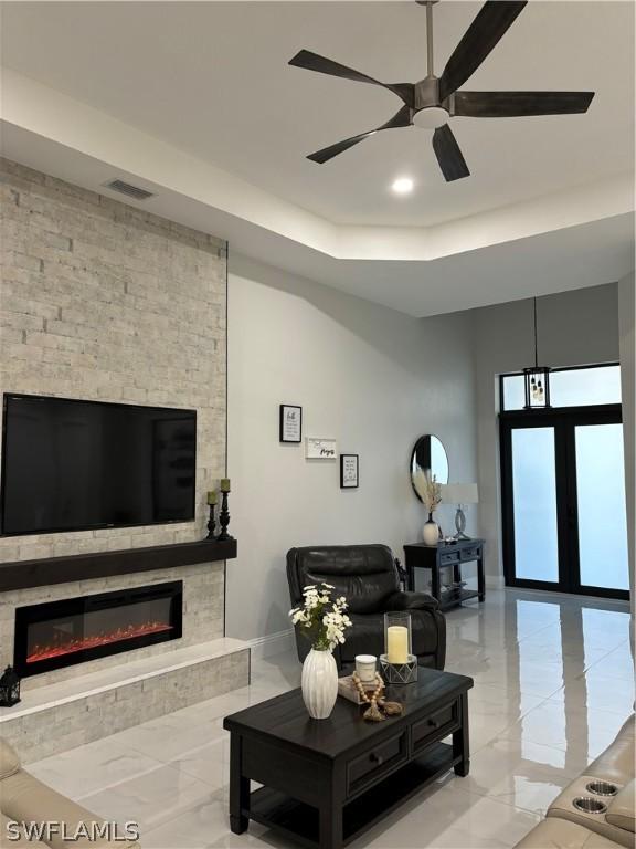 living room with ceiling fan, a fireplace, and a tray ceiling