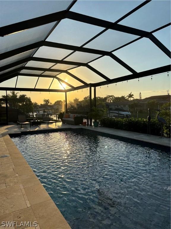 pool at dusk featuring an outdoor living space, a patio, and a lanai