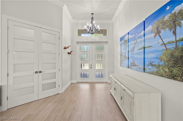 entrance foyer with light hardwood / wood-style floors, a notable chandelier, crown molding, and french doors