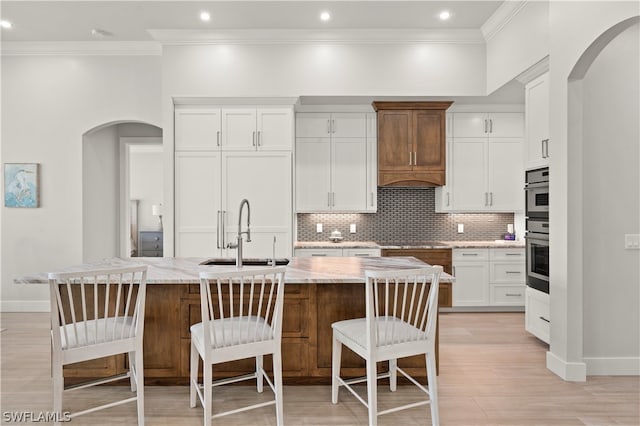 kitchen with light stone counters, sink, white cabinets, and an island with sink