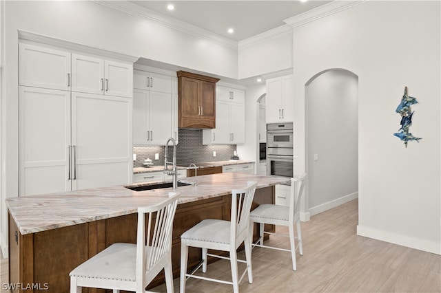 kitchen featuring white cabinetry, an island with sink, a kitchen breakfast bar, light stone countertops, and sink