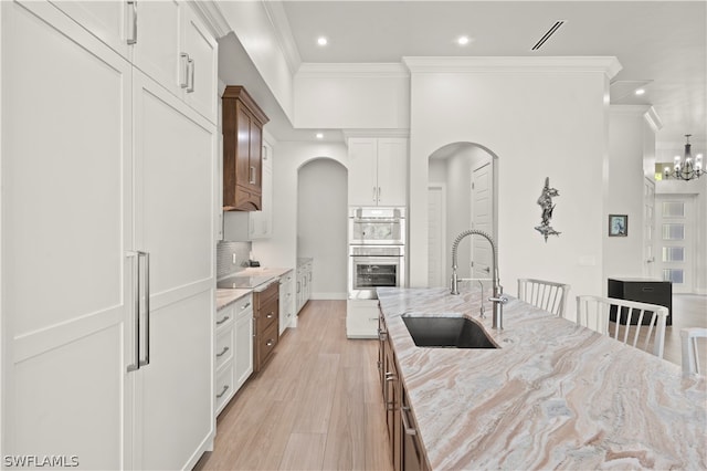 kitchen with tasteful backsplash, sink, white cabinetry, light stone countertops, and stainless steel double oven