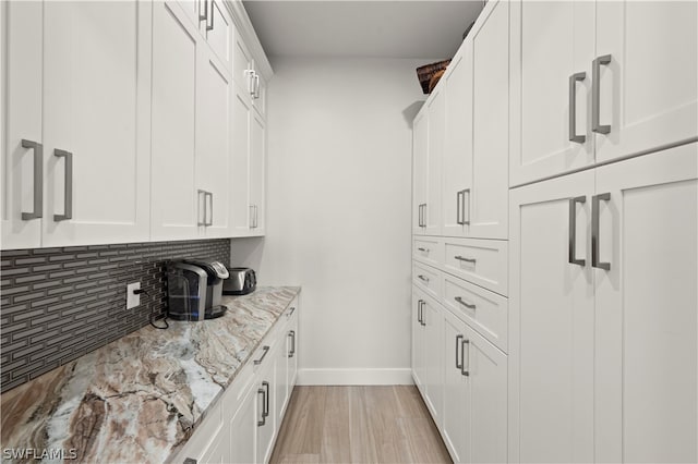 kitchen with tasteful backsplash, white cabinets, light wood-type flooring, and light stone counters