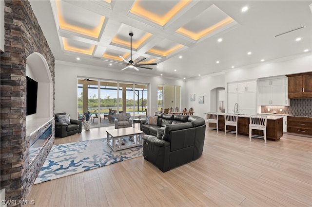 living room featuring ceiling fan, light wood-type flooring, coffered ceiling, and ornamental molding