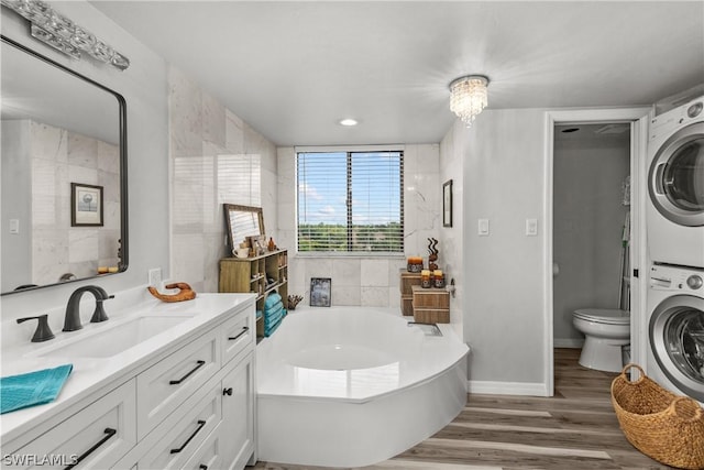 bathroom with vanity, hardwood / wood-style flooring, stacked washer / dryer, toilet, and a tub