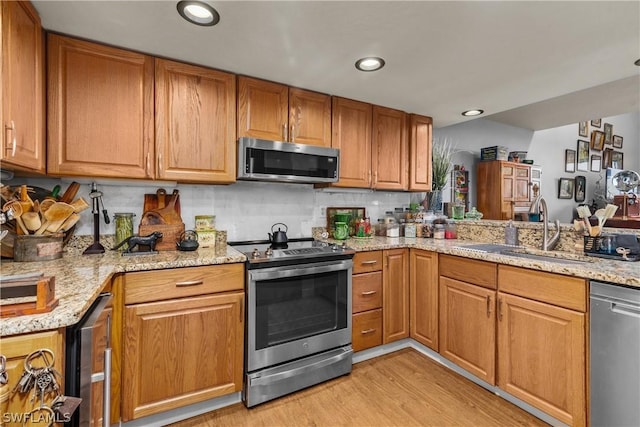 kitchen featuring light stone countertops, sink, light hardwood / wood-style flooring, decorative backsplash, and appliances with stainless steel finishes