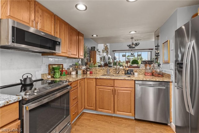 kitchen with backsplash, sink, light wood-type flooring, light stone counters, and stainless steel appliances