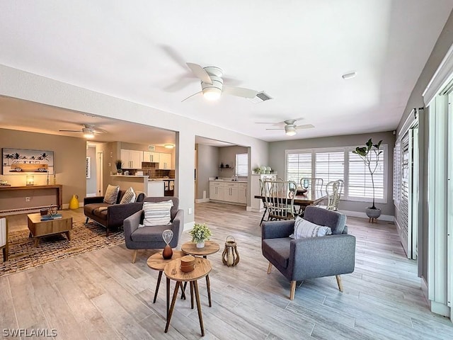 living area featuring a ceiling fan, baseboards, and light wood-style floors